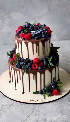 a three tiered cake with berries and chocolate drizzled on the top