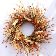 a wreath is hanging on the door with dried flowers and leaves around it in front of a white door