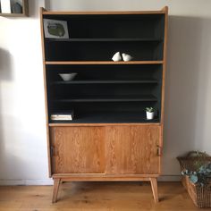 a wooden bookcase with black shelves and white bowls on top, next to a basket