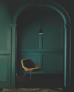 a yellow chair sitting in front of a green wall with an arched doorway and floor lamp