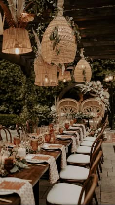 an outdoor dining area with wicker hanging lights and rattan - like chairs, white tablecloths on the tables