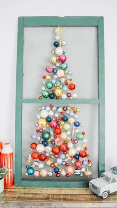 a christmas tree made out of ornaments is displayed in front of an old window frame