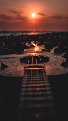 an acoustic guitar laying on the ground at sunset