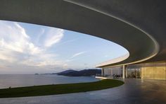 an outdoor area with grass and water next to the ocean at dusk or dawn, as seen from under a curved concrete structure