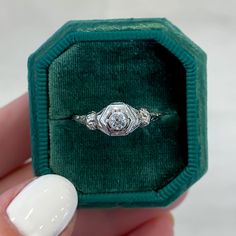 a woman's hand holding an engagement ring in a green velvet box