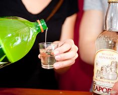 a woman pours a drink from a green pitcher into a glass at a bar