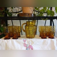 an assortment of glassware on a table with plants in the backgroung