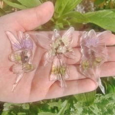 three tiny plastic flowers in the palm of someone's hand with green leaves behind them