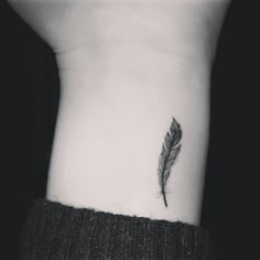 a black and white photo of a small feather tattoo on the left side of the wrist