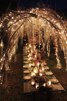 a long table with candles on it under an arch covered in fairy lights and branches