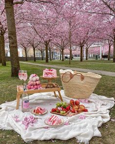 a picnic with food and drinks on the grass in front of cherry blossom covered trees