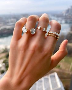 a woman's hand holding three rings in front of her face, with the city behind her