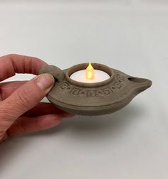 a hand holding a small clay tea light holder with a lit candle in the middle