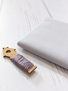 a piece of fabric next to a sewing needle on a white wooden table with a gray pillow