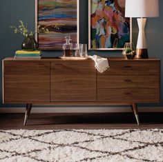 a living room with two paintings on the wall and a dresser in front of it