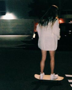 a woman riding a skateboard across a cross walk at night with her hair blowing in the wind