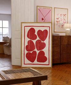 two framed art pieces sitting on top of a hard wood floor next to a wooden table