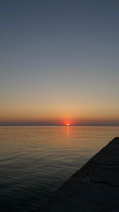 the sun is setting over the water at the end of a pier