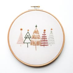 a cross stitch christmas tree pattern on a white wall hanging from a wooden hoop with an orange thread