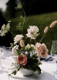 an arrangement of flowers and greenery in a vase on a table with wine glasses