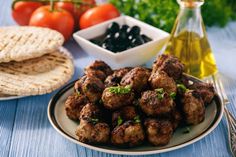 meatballs and olives on a plate next to pita bread, tomatoes, and oil