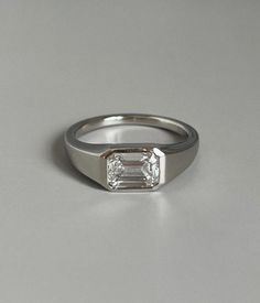 an engagement ring with a baguette cut diamond in the center on a grey background