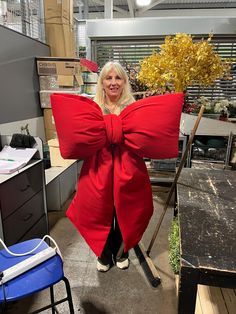 a woman in a red coat holding up a giant bow shaped pillow at an office