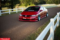 a red car driving down a road next to a white fence