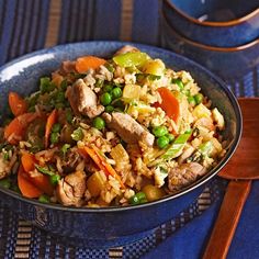 a blue bowl filled with rice, meat and veggies next to a wooden spoon