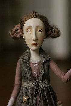 the doll is wearing a gray dress and brown jacket