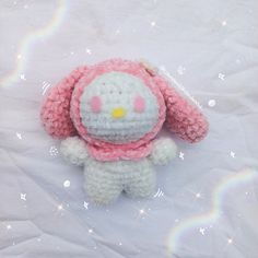 a crocheted hello kitty doll laying on top of a white sheet with rainbows in the background