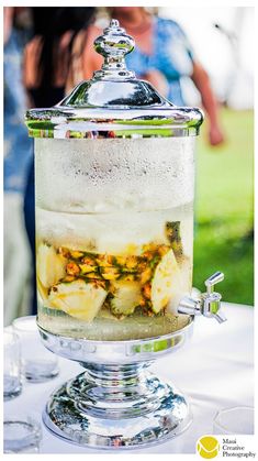 a glass jar filled with ice and fruit on top of a table next to people