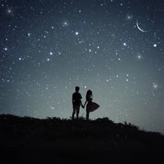 two people standing on top of a hill holding hands under the night sky with stars