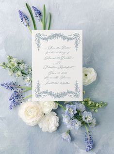 the wedding stationery is laid out on top of blue and white flowers, along with greenery