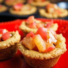 small cupcakes with fruit on top are sitting on a red plate in front of other pastries