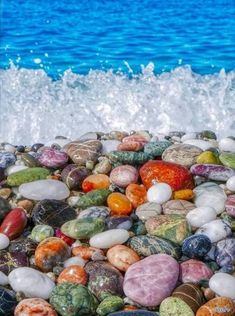 many different colored rocks on the beach next to the ocean with waves crashing over them