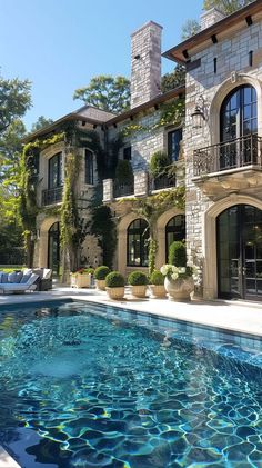 an outdoor swimming pool in front of a large house with stone columns and windows on the side