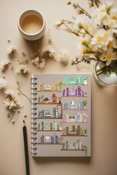 a spiral notebook sitting on top of a table next to a cup of coffee and flowers