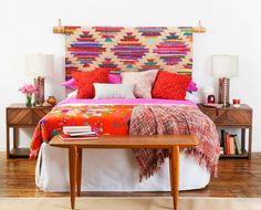 a bed with colorful blankets and pillows in a white room next to two nightstands