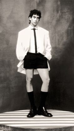 black and white photograph of man in dress shirt and tie standing on top of a stool