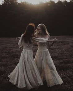 two women in long dresses are standing in a field at sunset or sunrise, with the sun shining behind them