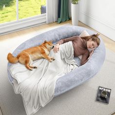 a woman laying in a dog bed on the floor next to a brown and white dog