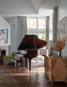 a living room with a grand piano in the center and paintings on the wall behind it