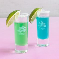 two glasses filled with blue and green liquid next to each other on a pink surface