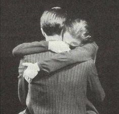 two people hugging each other in front of a black background