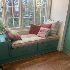 a window seat with many pillows on it in front of a green cabinet and wooden floor