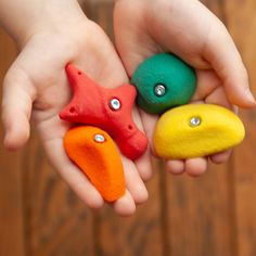 two hands holding three different colored rocks with diamond eyes and one starfish on each hand