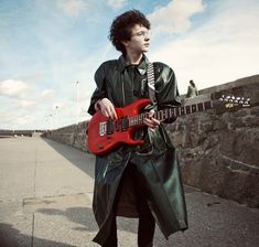 a man in green raincoat playing an electric guitar on the side of a road