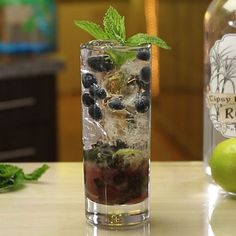 a glass filled with ice and blackberries next to a bottle of ginzetti