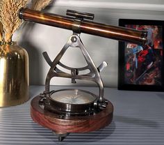 an old fashioned telescope sitting on top of a table next to a vase with dried flowers